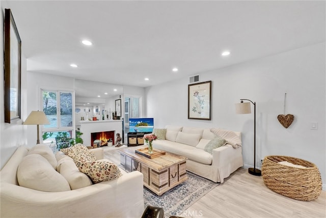 living area with a warm lit fireplace, recessed lighting, visible vents, and light wood-style floors