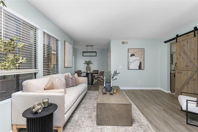 living area with wood finished floors, visible vents, baseboards, and a barn door