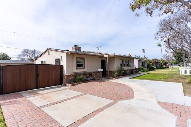 view of front of house with stucco siding, a gate, fence, brick siding, and a chimney