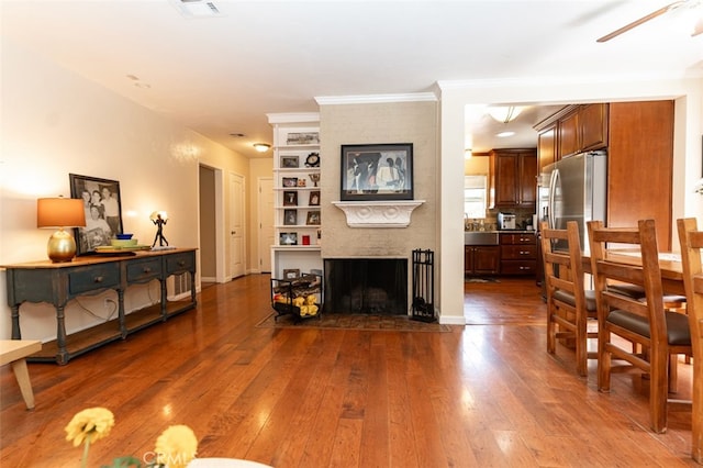 living room featuring visible vents, dark wood-type flooring, a ceiling fan, a large fireplace, and baseboards