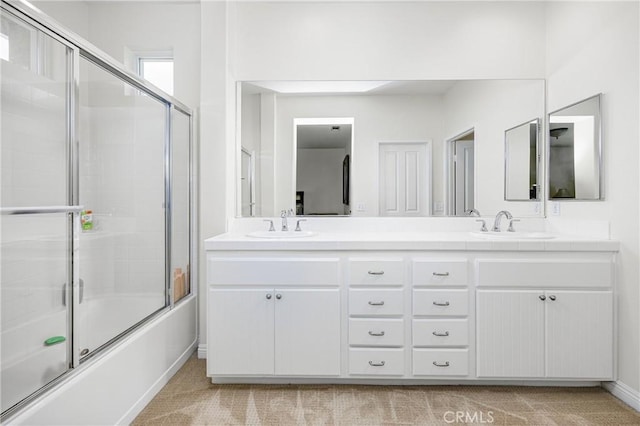 bathroom with double vanity, combined bath / shower with glass door, baseboards, and a sink
