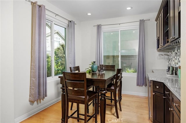 dining area featuring recessed lighting, light wood-style floors, a bar, and baseboards