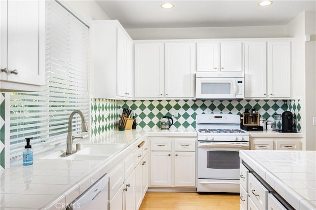 kitchen with white cabinetry, tile counters, a sink, and white appliances