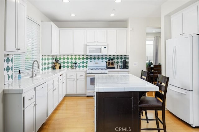 kitchen featuring light wood finished floors, backsplash, tile countertops, white appliances, and a center island