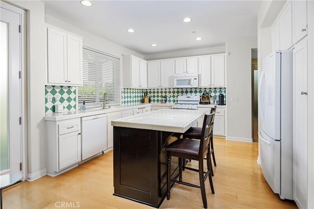 kitchen with light wood finished floors, white appliances, tile countertops, and tasteful backsplash
