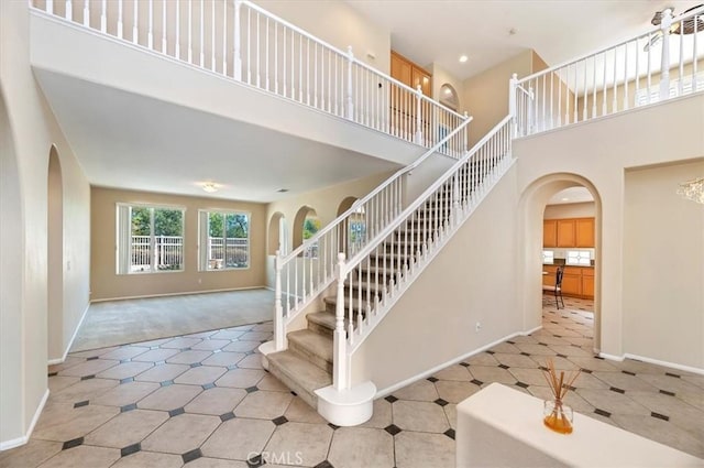 staircase featuring baseboards, a high ceiling, and arched walkways