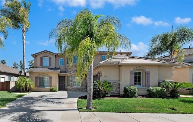 mediterranean / spanish home with driveway, stone siding, a tiled roof, fence, and stucco siding