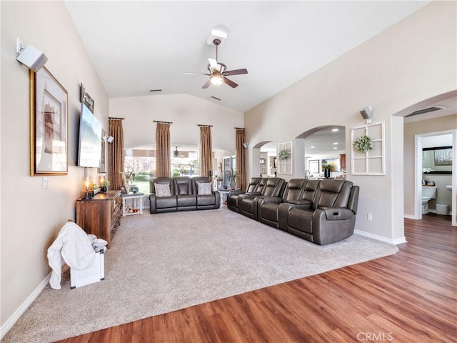 carpeted living area featuring a ceiling fan, arched walkways, baseboards, and wood finished floors