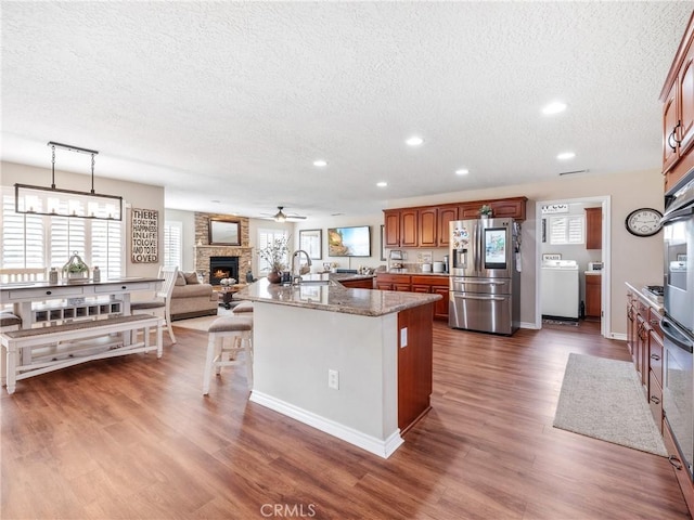 kitchen featuring dark wood finished floors, a fireplace, washer / clothes dryer, brown cabinetry, and stainless steel fridge with ice dispenser