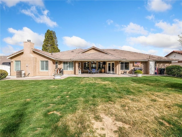 back of property featuring a patio, central AC, a lawn, stucco siding, and a chimney