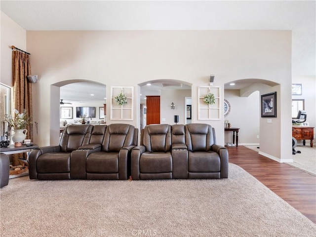 carpeted living room featuring a towering ceiling, baseboards, arched walkways, and wood finished floors