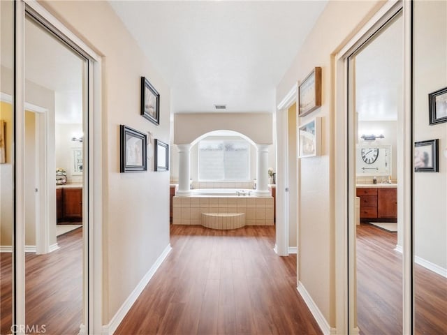 hall featuring arched walkways, decorative columns, visible vents, wood finished floors, and baseboards