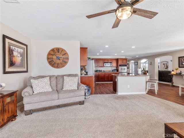 living area featuring arched walkways, a ceiling fan, dark colored carpet, a textured ceiling, and recessed lighting