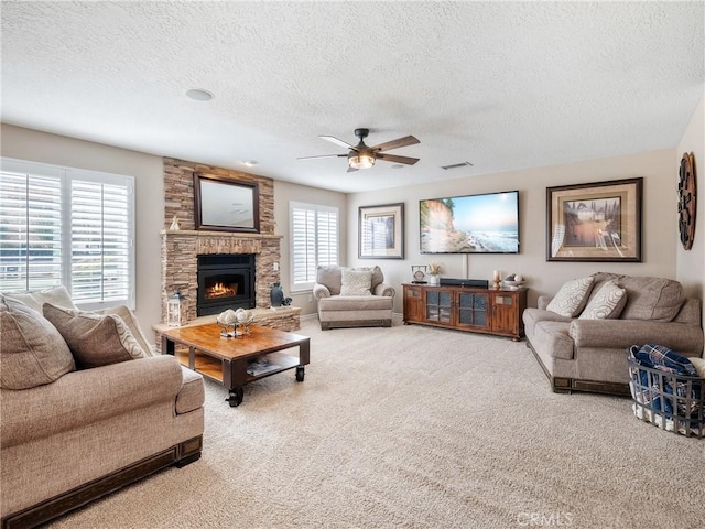 carpeted living area featuring a textured ceiling, a stone fireplace, visible vents, and a ceiling fan