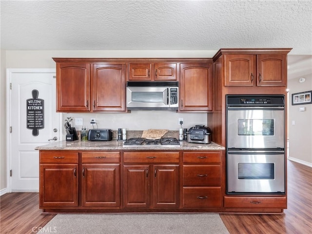 kitchen featuring a textured ceiling, appliances with stainless steel finishes, dark wood finished floors, and light stone counters