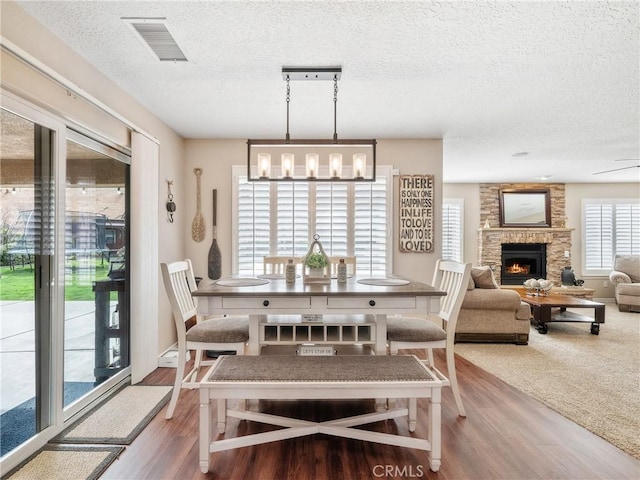 dining area with visible vents, wood finished floors, a textured ceiling, a fireplace, and a chandelier