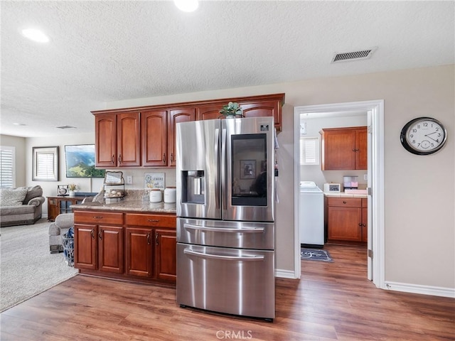 kitchen featuring washer / clothes dryer, visible vents, stainless steel fridge with ice dispenser, and wood finished floors