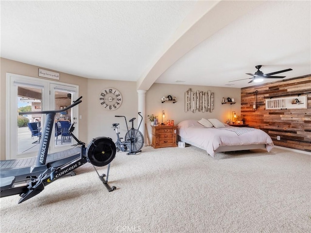 carpeted bedroom featuring ceiling fan, wooden walls, a textured ceiling, and decorative columns