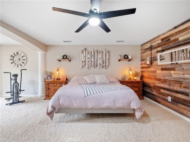 bedroom with wooden walls, visible vents, carpet flooring, a textured ceiling, and ornate columns