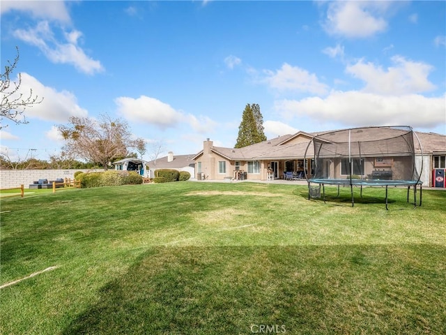 rear view of property with a trampoline, a patio area, and a lawn