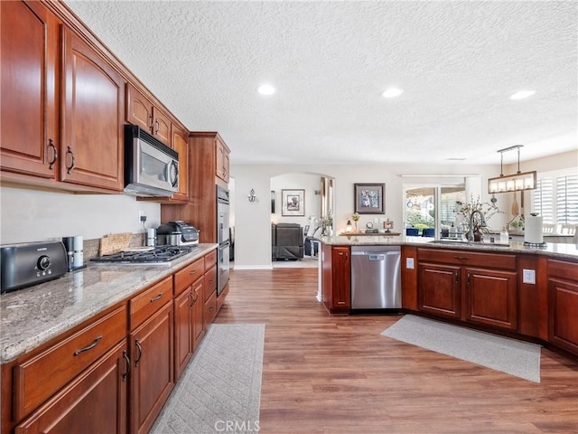 kitchen with light stone counters, hanging light fixtures, appliances with stainless steel finishes, a sink, and wood finished floors