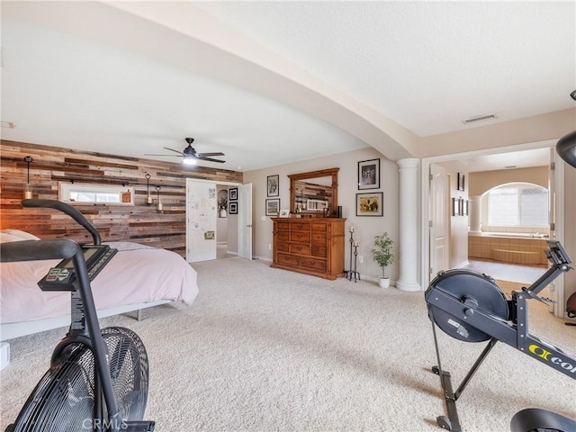 carpeted bedroom with wooden walls, an accent wall, visible vents, baseboards, and decorative columns