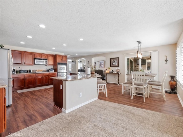 kitchen with appliances with stainless steel finishes, arched walkways, dark wood-type flooring, and recessed lighting