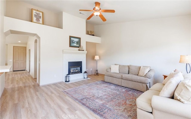 living room featuring visible vents, arched walkways, a ceiling fan, a glass covered fireplace, and light wood-style flooring