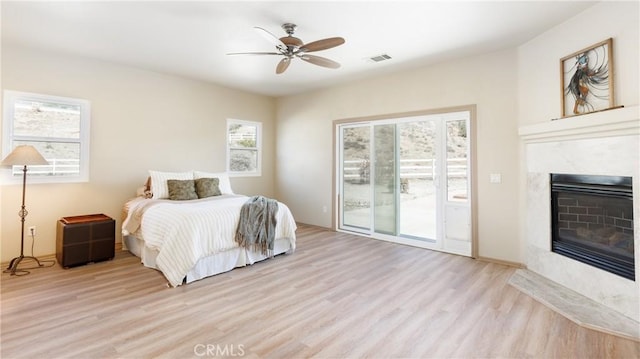 bedroom with ceiling fan, a high end fireplace, visible vents, light wood-style floors, and access to outside