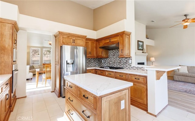 kitchen with tasteful backsplash, appliances with stainless steel finishes, open floor plan, a peninsula, and under cabinet range hood