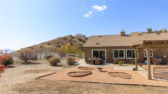 rear view of property featuring fence, a tile roof, stucco siding, a chimney, and a patio area