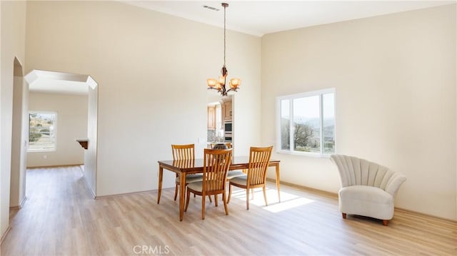 dining space featuring a towering ceiling, light wood-style floors, visible vents, and a notable chandelier