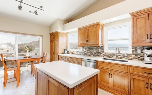 kitchen with a sink, vaulted ceiling, light countertops, stainless steel dishwasher, and backsplash