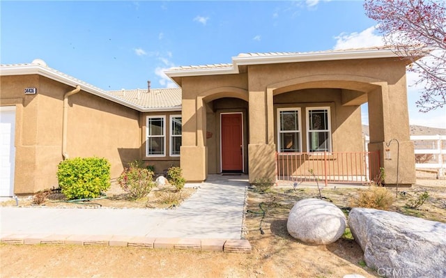 entrance to property with an attached garage, covered porch, a tiled roof, and stucco siding