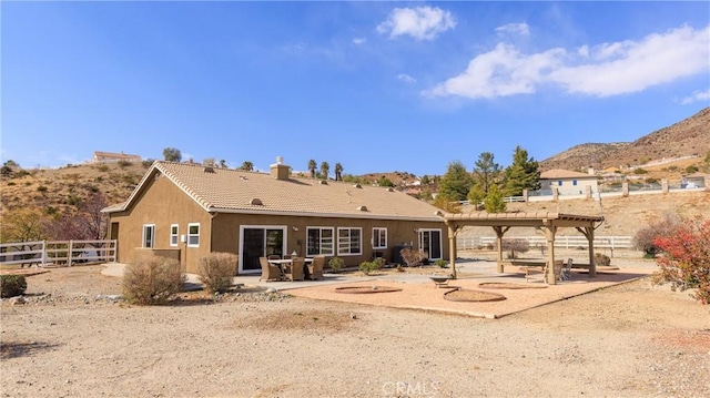 rear view of house with a tile roof, a chimney, stucco siding, a patio area, and fence