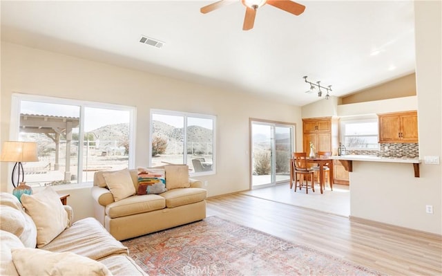 living area featuring visible vents, vaulted ceiling, a wealth of natural light, and light wood-style floors