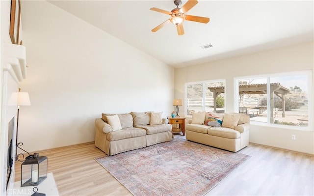 living room featuring a ceiling fan, vaulted ceiling, a fireplace with flush hearth, and wood finished floors