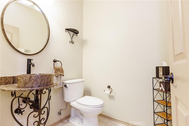 half bathroom featuring toilet, baseboards, a sink, and tile patterned floors