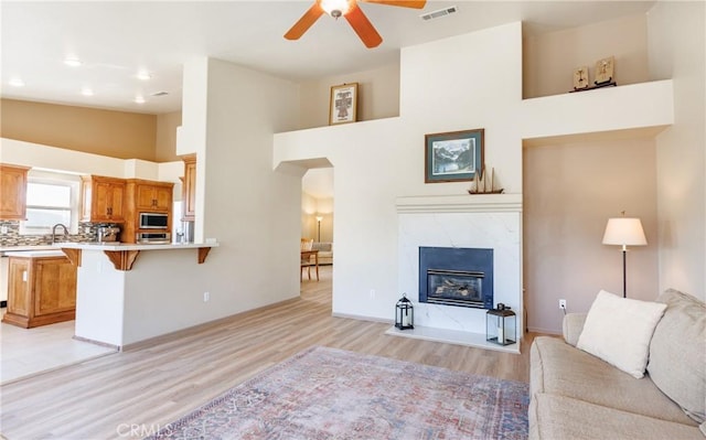 living area with visible vents, arched walkways, light wood-style flooring, high vaulted ceiling, and a high end fireplace