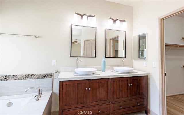 full bath featuring a garden tub, double vanity, wood finished floors, and a sink