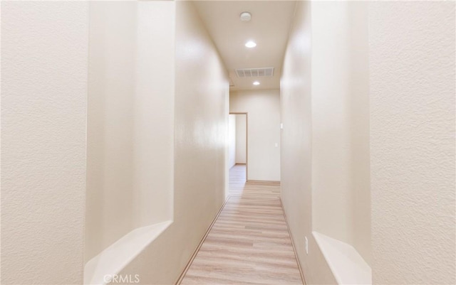 hallway with a textured wall, light wood-type flooring, visible vents, and recessed lighting