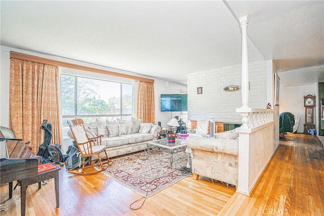 living area with a textured ceiling, wood finished floors, and ornate columns