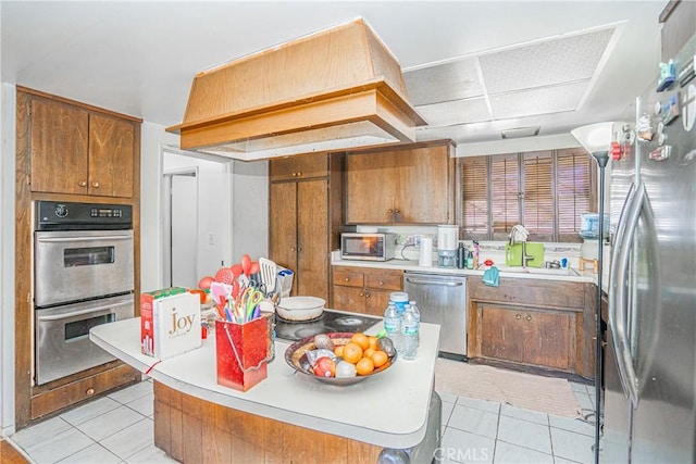 kitchen featuring light tile patterned floors, a sink, appliances with stainless steel finishes, brown cabinets, and custom range hood