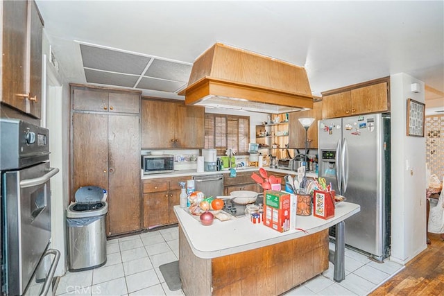 kitchen featuring brown cabinetry, custom exhaust hood, stainless steel appliances, and light countertops