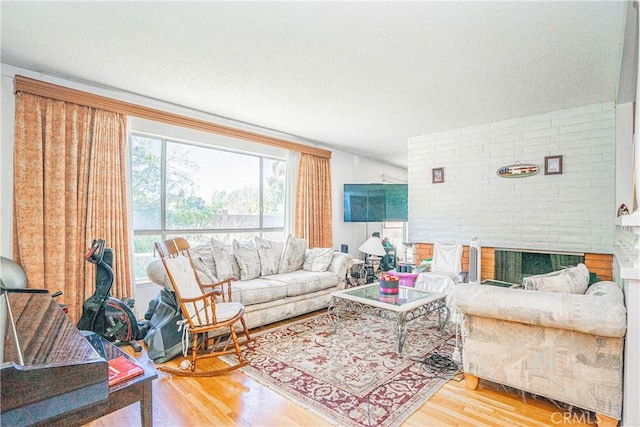 living area with a textured ceiling, a brick fireplace, and wood finished floors