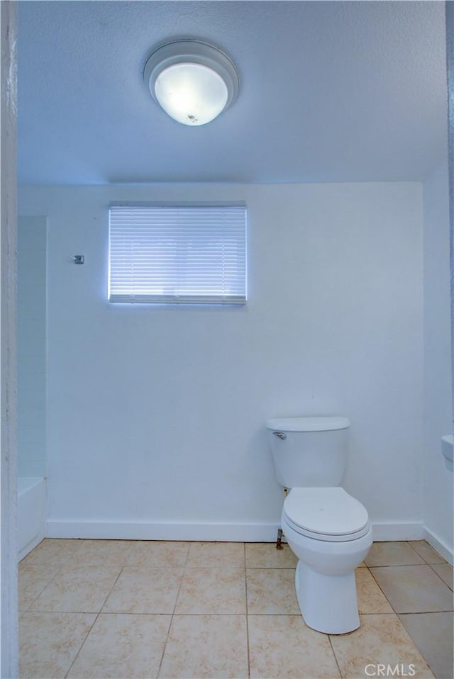 bathroom featuring a bath, baseboards, toilet, and tile patterned floors