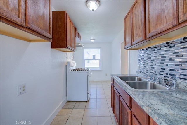 kitchen featuring light tile patterned floors, decorative backsplash, white gas range, under cabinet range hood, and a sink