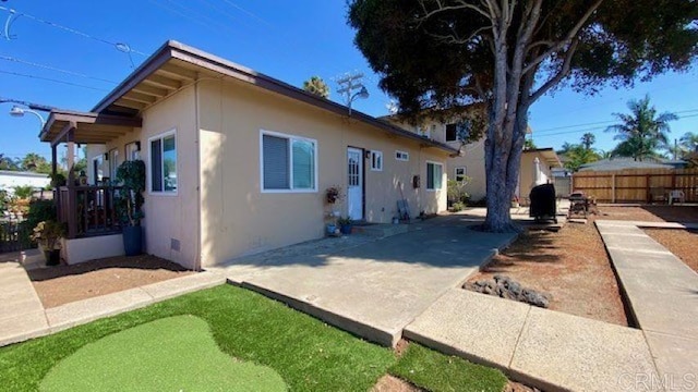 rear view of property featuring crawl space, a patio area, fence, and stucco siding