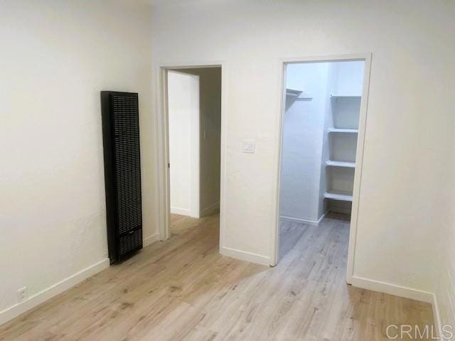 unfurnished bedroom featuring light wood-type flooring, a spacious closet, and baseboards