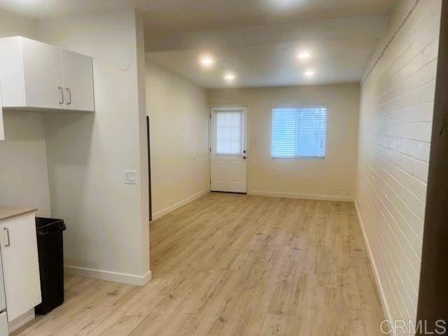 interior space featuring light wood finished floors, baseboards, white cabinets, brick wall, and light countertops